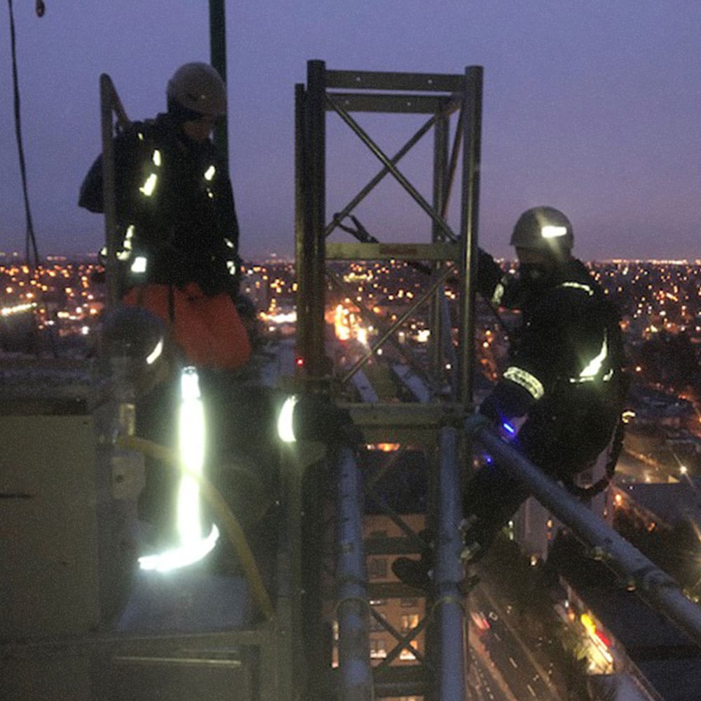 Two men setting tie-backs at the top of a tower