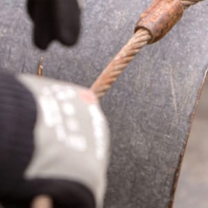 Close-up image of person's hand rigging a metal cable onto a large section of pipe.